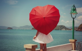海边手握红色心形雨伞的女孩