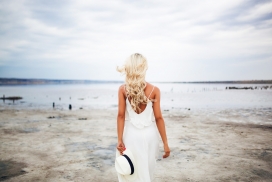 穿白色连衣裙手拿帽子的海边金发美女